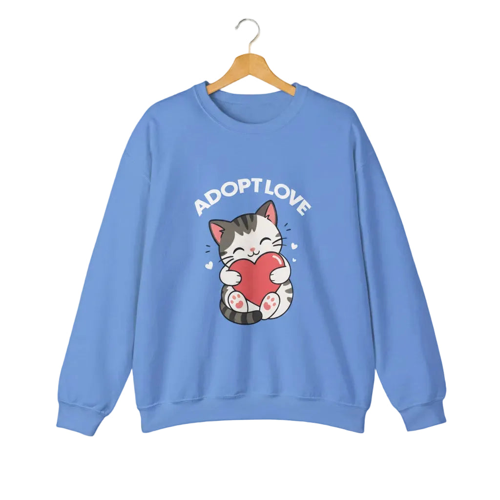 A carolina blue crewneck sweatshirt featuring a cartoon graphic of a gray tabby cat holding a red heart, with the text 'ADOPT LOVE' printed above it in white for cat lovers.