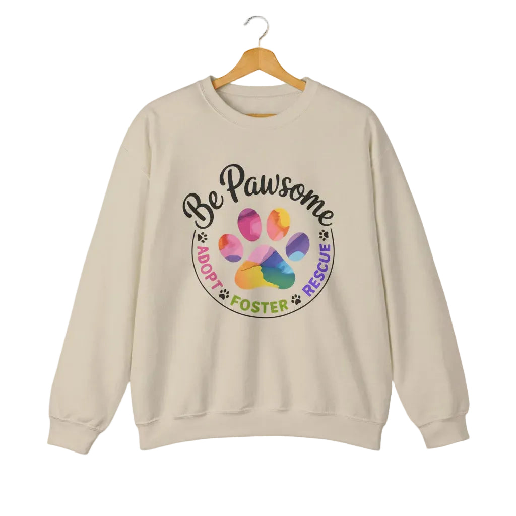Sand crewneck sweatshirt featuring a colorful paw print for cat rescue advocates with text 'Be Pawsome Adopt Foster Rescue'.
