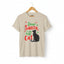 Sand short-sleeve t-shirt on a wooden hanger with green and red text saying "Dear Santa, it was the Cat" featuring a black cat silhouette.