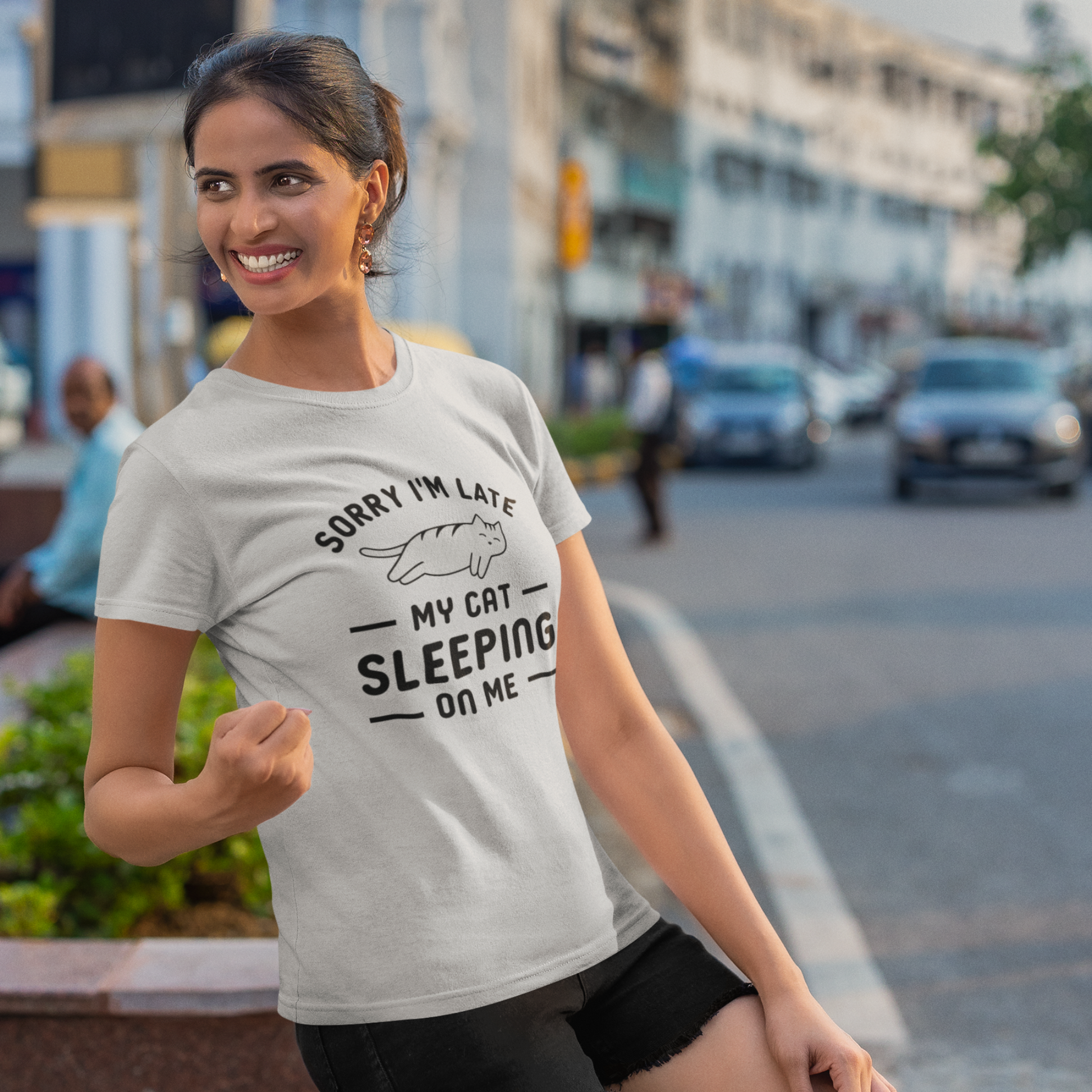 Woman modeling a white funny cat lover t-shirt featuring the quote "Sorry I'm Late, My Cat Was Sleeping on Me" with a cute sleeping cat graphic. Perfect gift for cat moms and cat lovers from Meow Paradise Store.