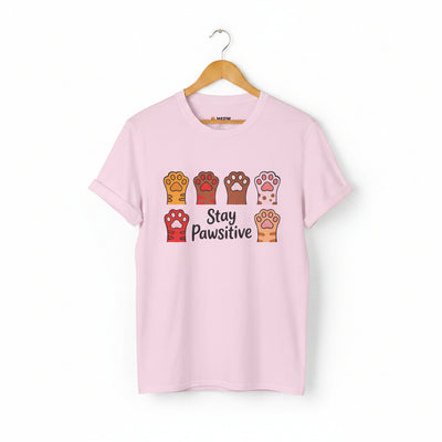 Light pink Stay Pawsitive t-shirt with colorful cat paws illustration for cat lovers.